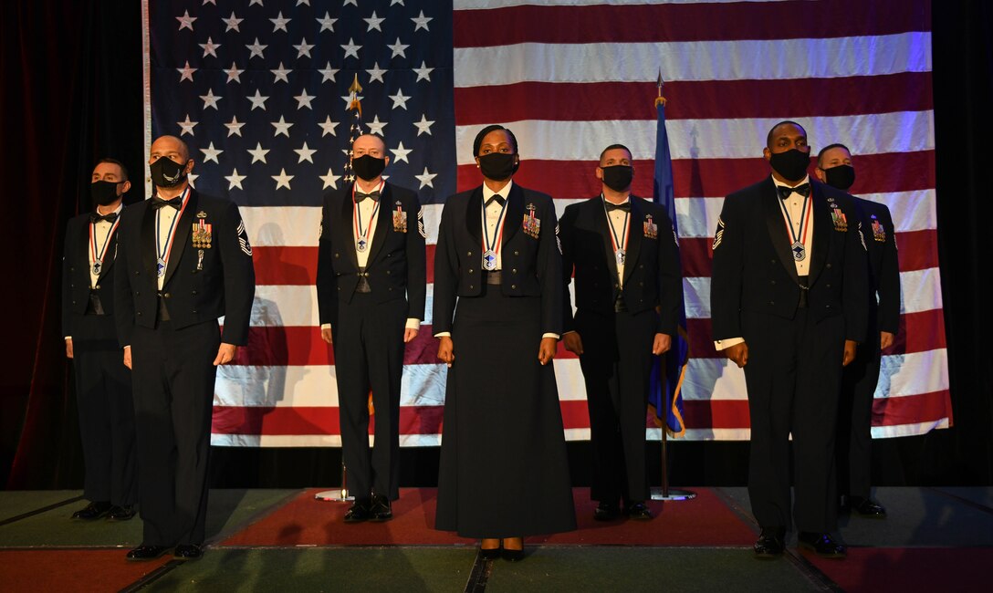 Seven Chief selects stand on a stage in their semi-formal dress uniform