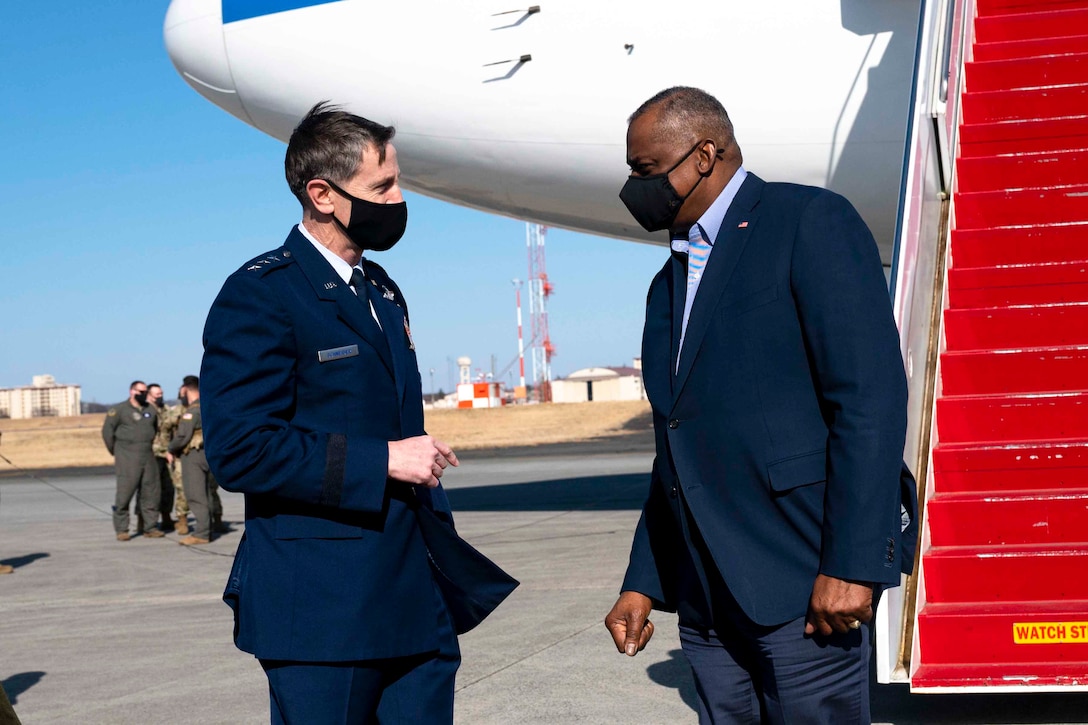 Secretary of Defense Lloyd J. Austin III stands facing an airman in front of a plane on a flightline.