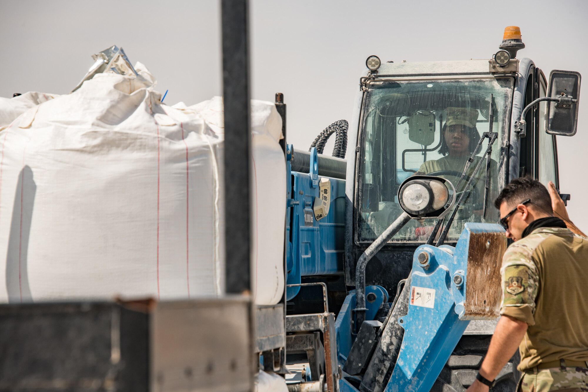 person in heavy machine lifts bag of concrete