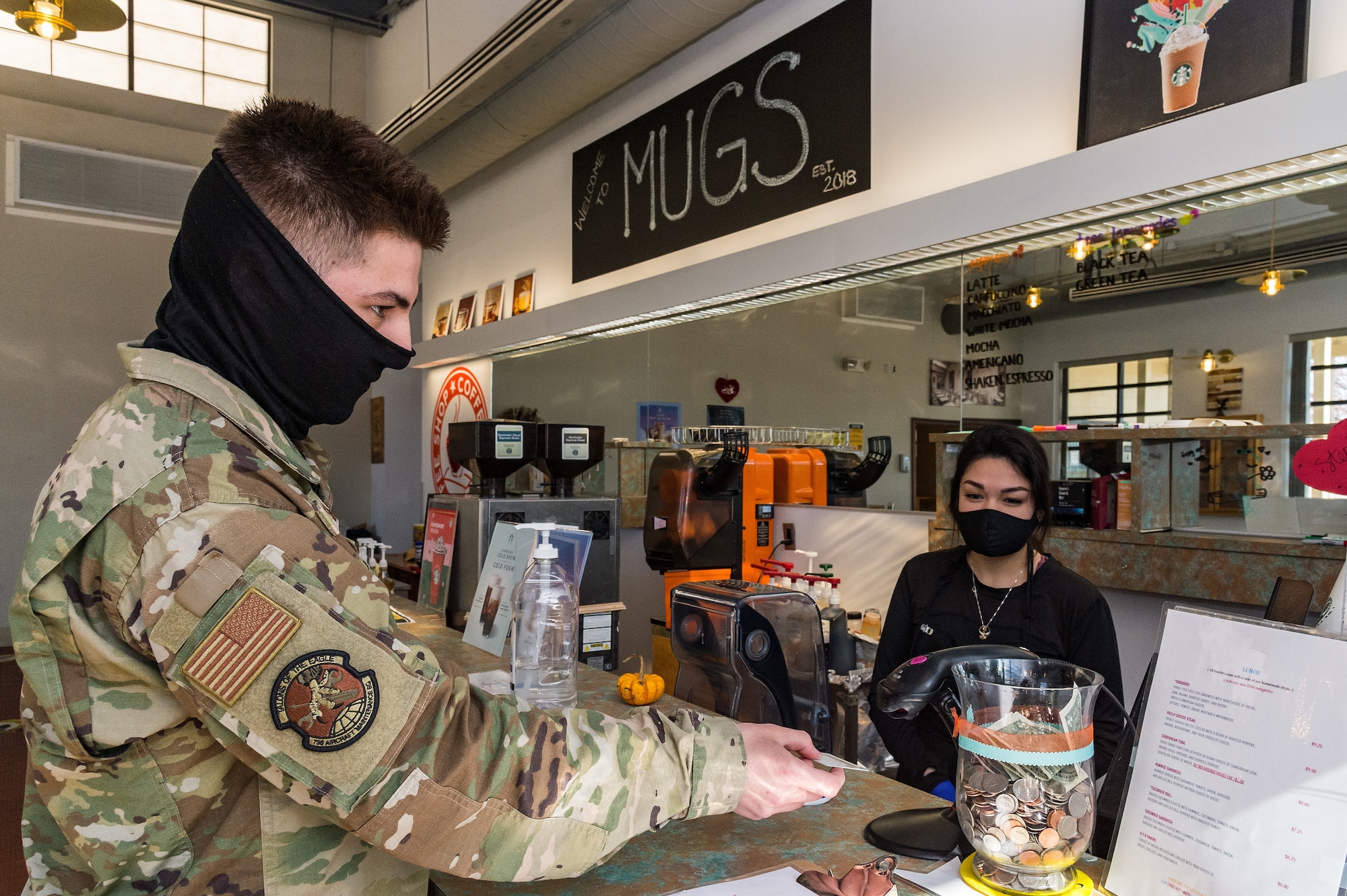 Airman Basic Eduardo Salcedo, 736th Aircraft Maintenance Squadron crew chief, scans his Common Access Card while Christine Paolini, 436th Force Support Squadron barista, watches as he  purchases food items at Mugs Coffee Bar on Dover Air Force Base, Delaware, March 15, 2021. Salcedo and other Airmen using their registered CAC for Essential Station Messing will have new dollar amounts for specific meals beginning April 1, 2021. Currently Mugs and FREDS are the only two nonappropriated fund food and beverage facilities where Airmen can purchase ESM eligible items. (U.S. Air Force photo by Roland Balik)