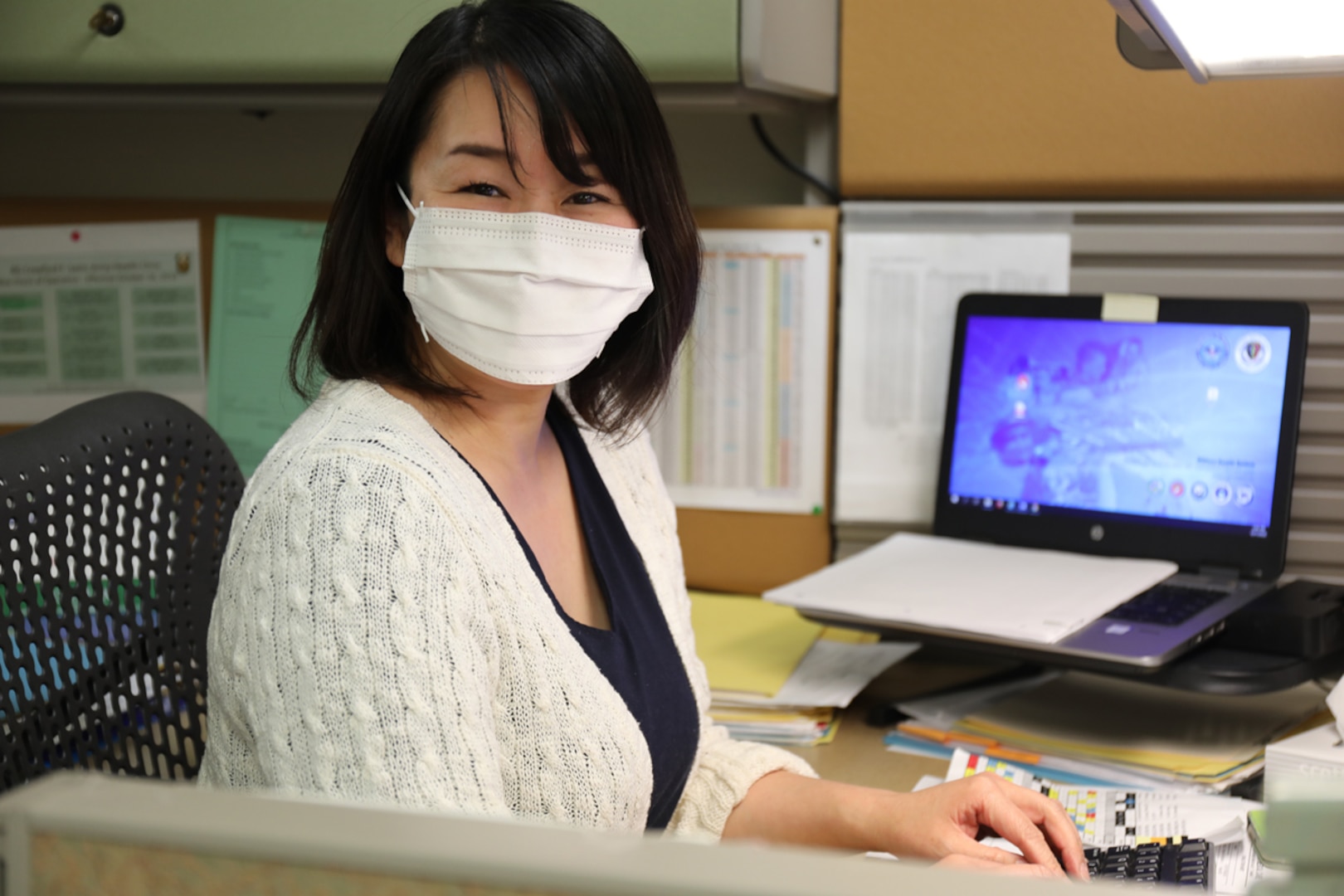 Woman sits at her desk and looks at camera