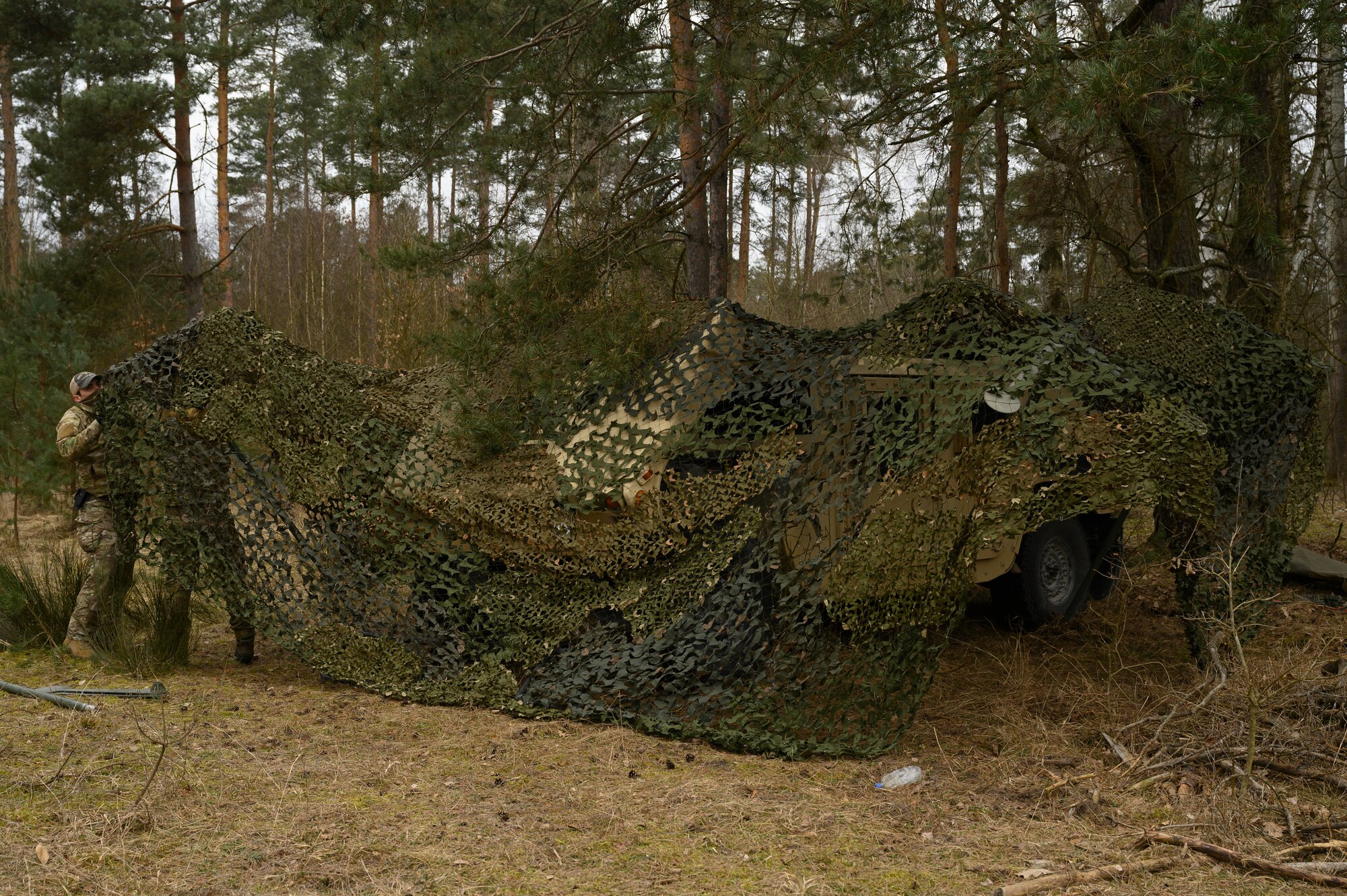 Airmen drap a camouflage net over a Humvee.