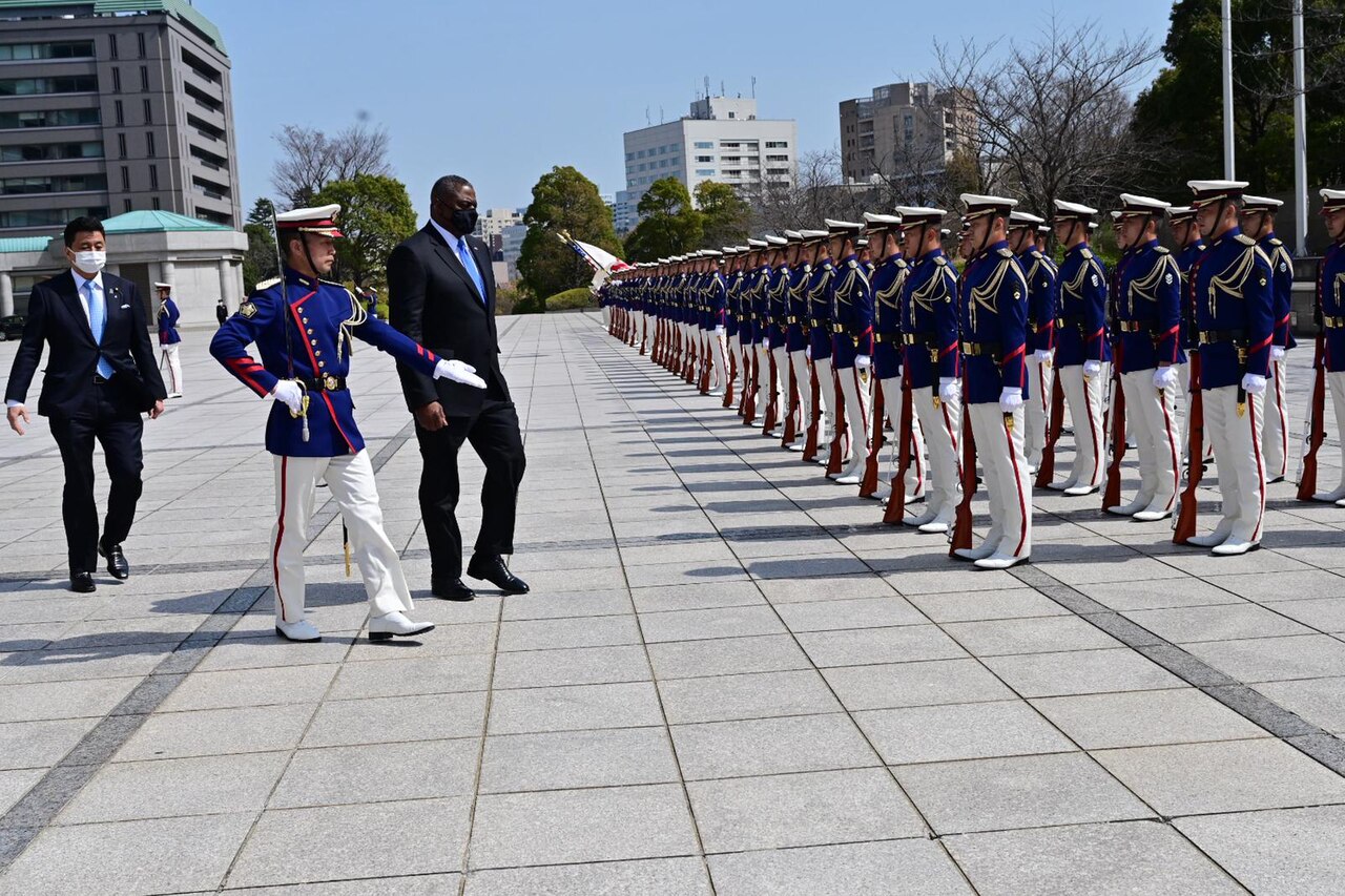 A soldier escorts a man in front of a military formation.