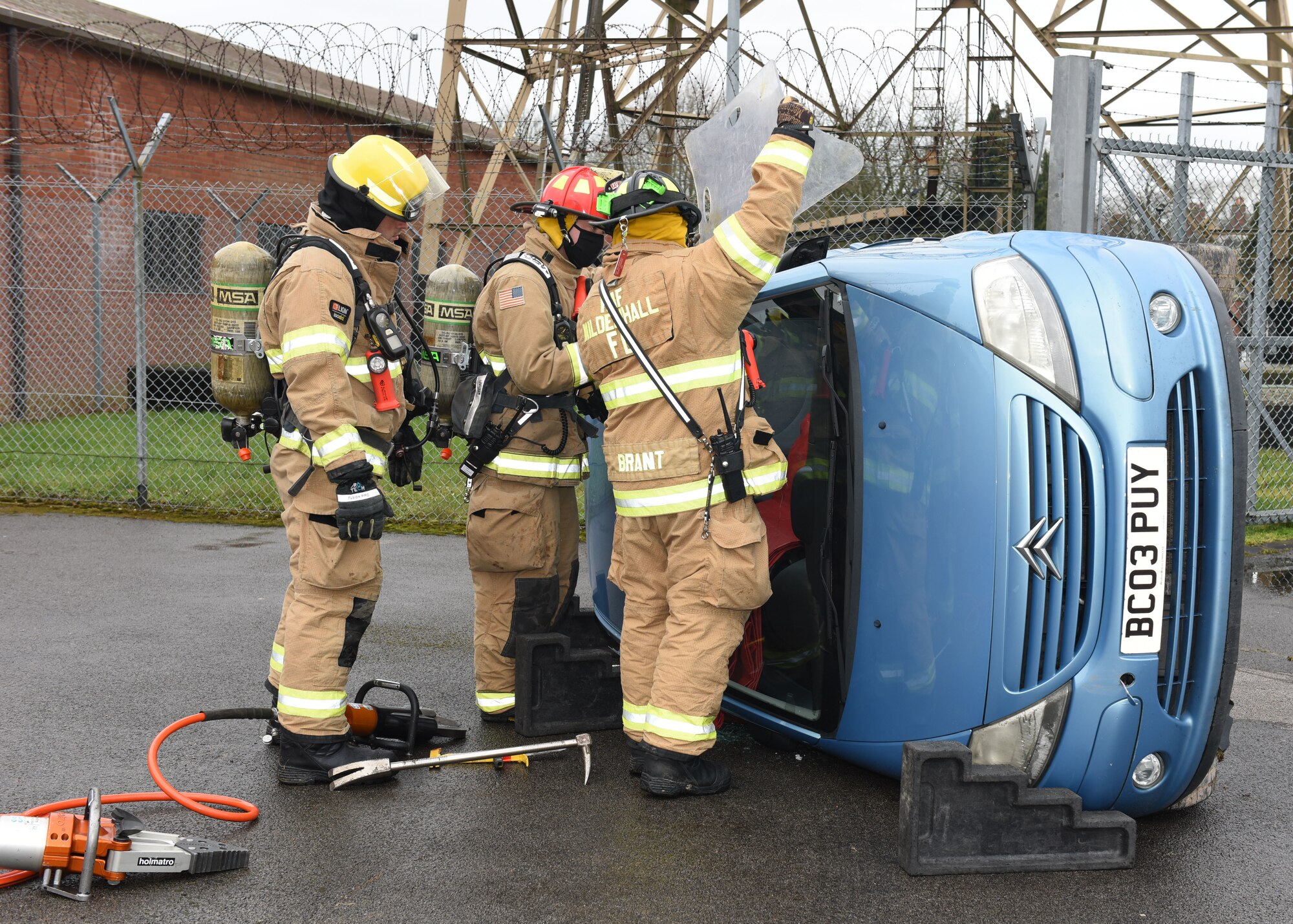 Firefighters from the 100th Civil Engineer Squadron Fire Department finish chocking a car and prepare to remove the windshield from an overturned car during a gate runner scenario as part of an exercise at Royal Air Force Mildenhall, England, March 16, 2021. The exercise was made up of a variety of scenarios to test the base’s emergency response and base defense for potential threats. (U.S. Air Force photo by Karen Abeyasekere)