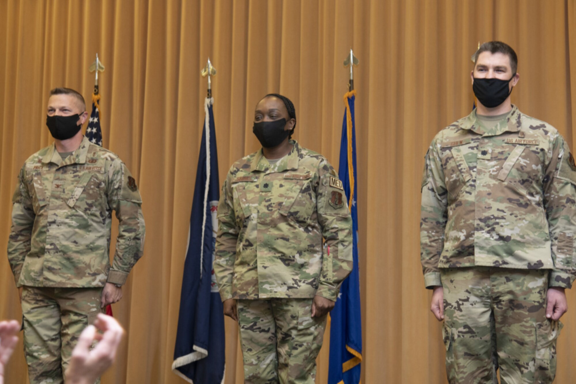 Three Airmen stand at attention in front  of flags
