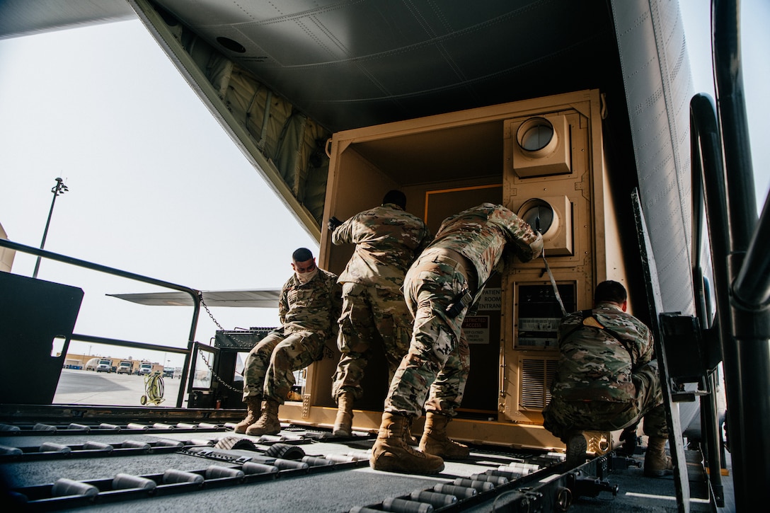 Four soldiers wearing face masks load a negatively pressurized conex onto an aircraft.