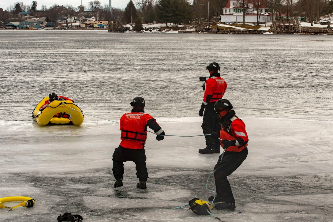 Coast Guardsmen pull a soldier to shore on a small boat from an icy body of water.