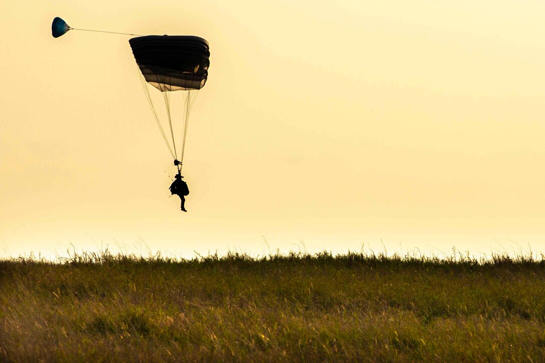 A Marine wearing a parachute descends in the sky.