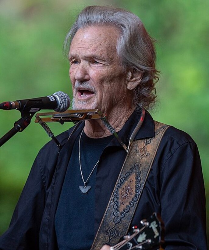 A singer with a guitar and standing at a microphone sings