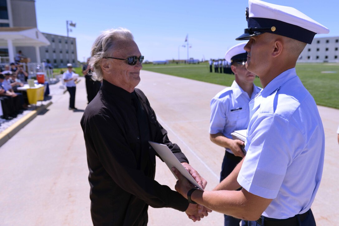 Two men, one in a military uniform, shake hands.