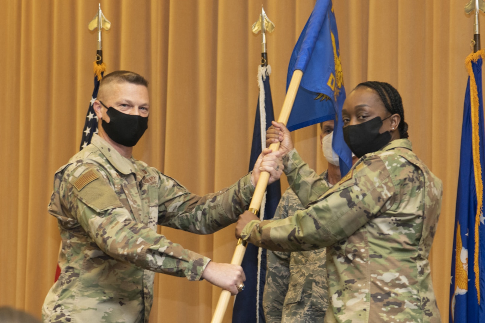 An airman hands a flag to another during a change of command ceremony