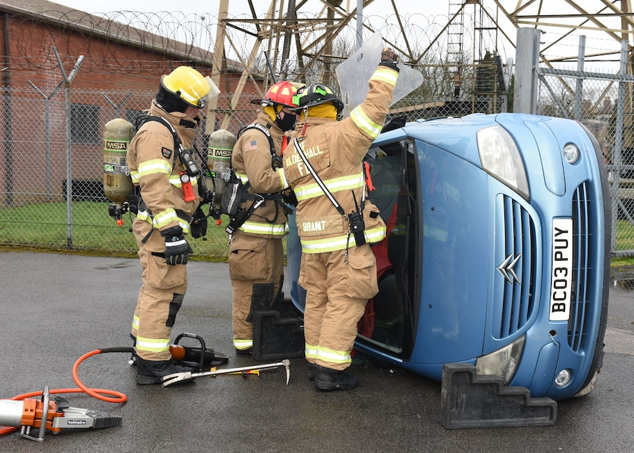 Firefighters from the 100th Civil Engineer Squadron Fire Department finish chocking a car and prepare to remove the windshield from an overturned car during a gate runner scenario as part of an exercise at Royal Air Force Mildenhall, England, March 16, 2021. The exercise was made up of a variety of scenarios to test the base’s emergency response and base defense for potential threats. (U.S. Air Force photo by Karen Abeyasekere)