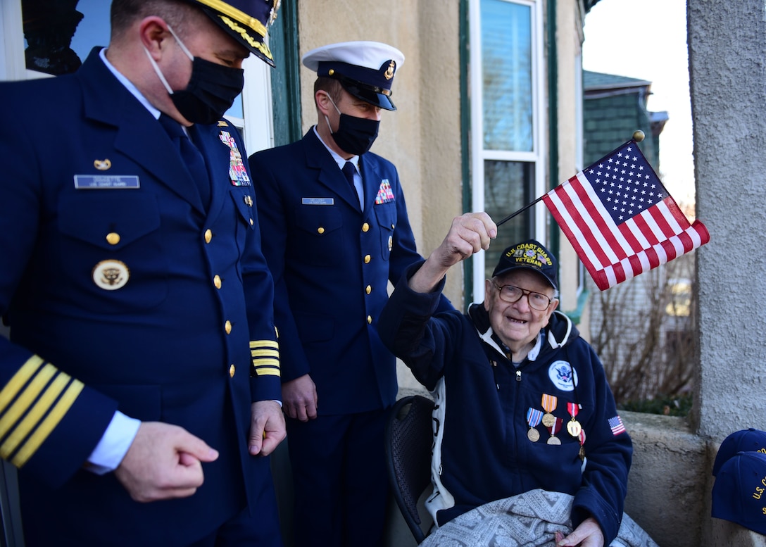 Capt. Eric Doucette and Senior Chief Petty Officer Christopher Melleby stand with Coast Guard-veteran Marvin Spitzer at his Boston home, February 26, 2021. Spitzer is celebrating his 100th birthday with a drive-by parade . (U.S. Coast Guard photo by Petty Officer 2nd Class Amanda Wyrick/Released)