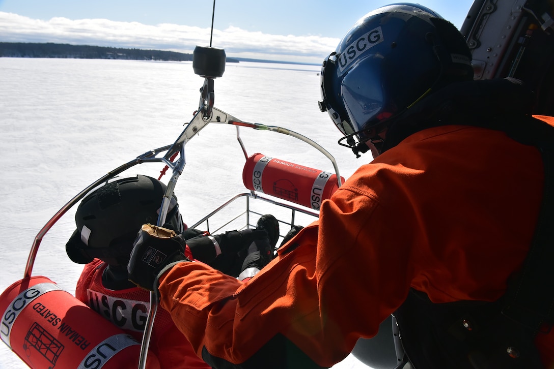 Petty Officer 2nd Class Zach Wilhelms, an avionics electrical technician serving as flight mechanic on an MH-60T Jayhawk helicopter, prepares to lower a trainee from Station Portage while conducting ice rescue training near Houghton, Mich. March 4, 2021. The training was designed to familiarize station personnel with hoisting procedures. U.S. Coast Guard photo by Chief Petty Officer John Masson.