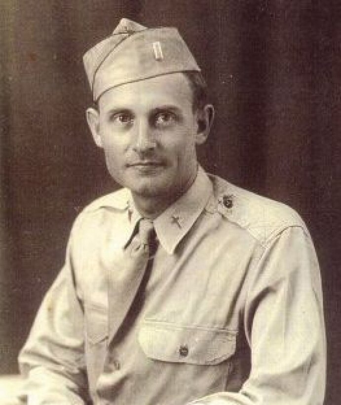 A young man in military shirt, tie and cap looks at the camera.