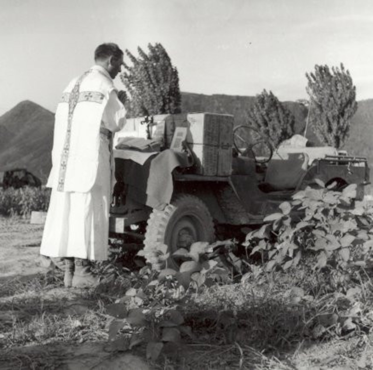 A priest prays toward an outdoor altar built on a Jeep.
