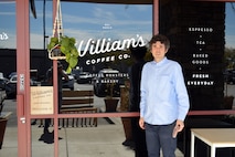 man in blue shirt standing in front of store front window of a coffee shop.