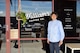 man in blue shirt standing in front of store front window of a coffee shop.