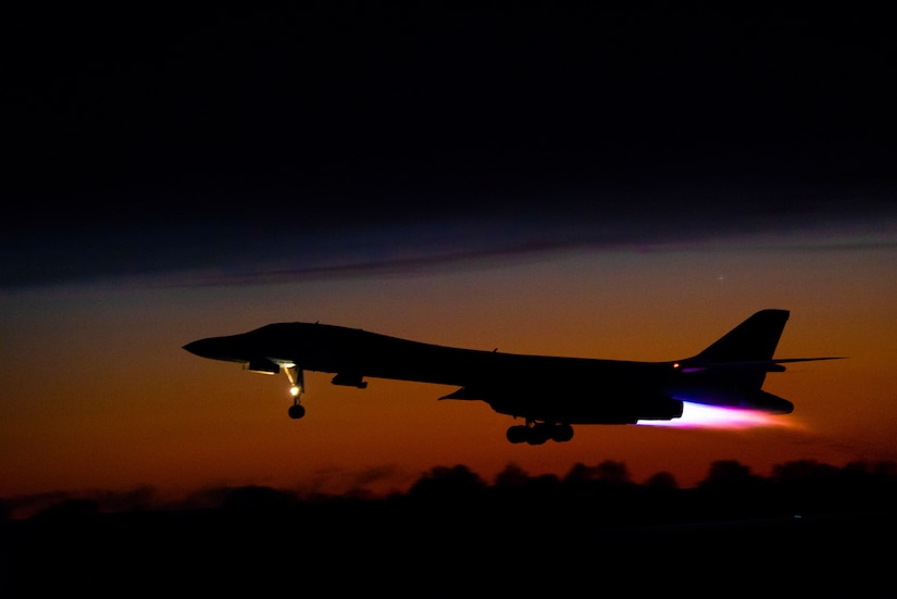 A B-1B Lancer aircraft takes off in front of a sunset.