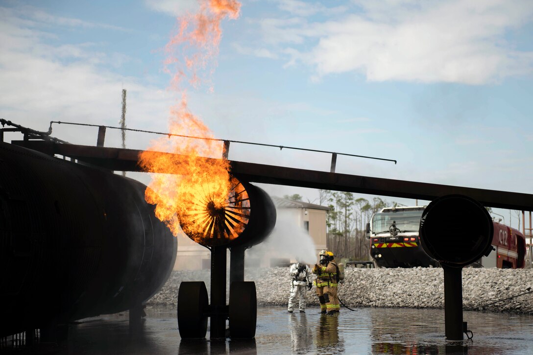 Airmen use a water hose to put out a fire on a simulated aircraft.