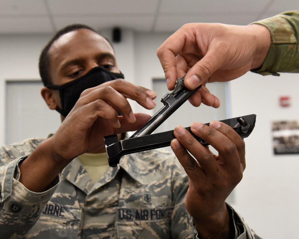 Air Force SSgt. Stephen Osborne, an 88th Health Care Operations Squadron respiratory therapist, reassembles his M9 pistol with a hand from Senior Airman Jerome Fogg, an 88th Security Forces Squadron combat arms instructor, during a qualification course at Wright-Patterson Air Force Base, Ohio on Feb. 18, 2021. Weapons qualification is part of the readiness standards for the 88th Air Base Wing. No live ammunition is allowed in the classroom portion of the qualification course. (U.S. Air Force photo by Ty Greenlees)