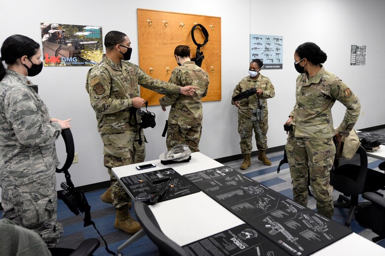 Air Force Senior Airman Jerome Fogg, an 88th Security Forces Squadron combat arms instructor, assists trainees with M9 pistol holsters during a qualification course at Wright-Patterson Air Force Base, Ohio on Feb. 18, 2021. Weapons qualification is part of the readiness standards for the 88th Air Base Wing. No live ammunition is allowed in the classroom portion of the qualification course. (U.S. Air Force photo by Ty Greenlees