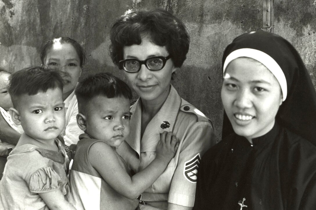 A Marine holds two babies while sitting next to a nun.