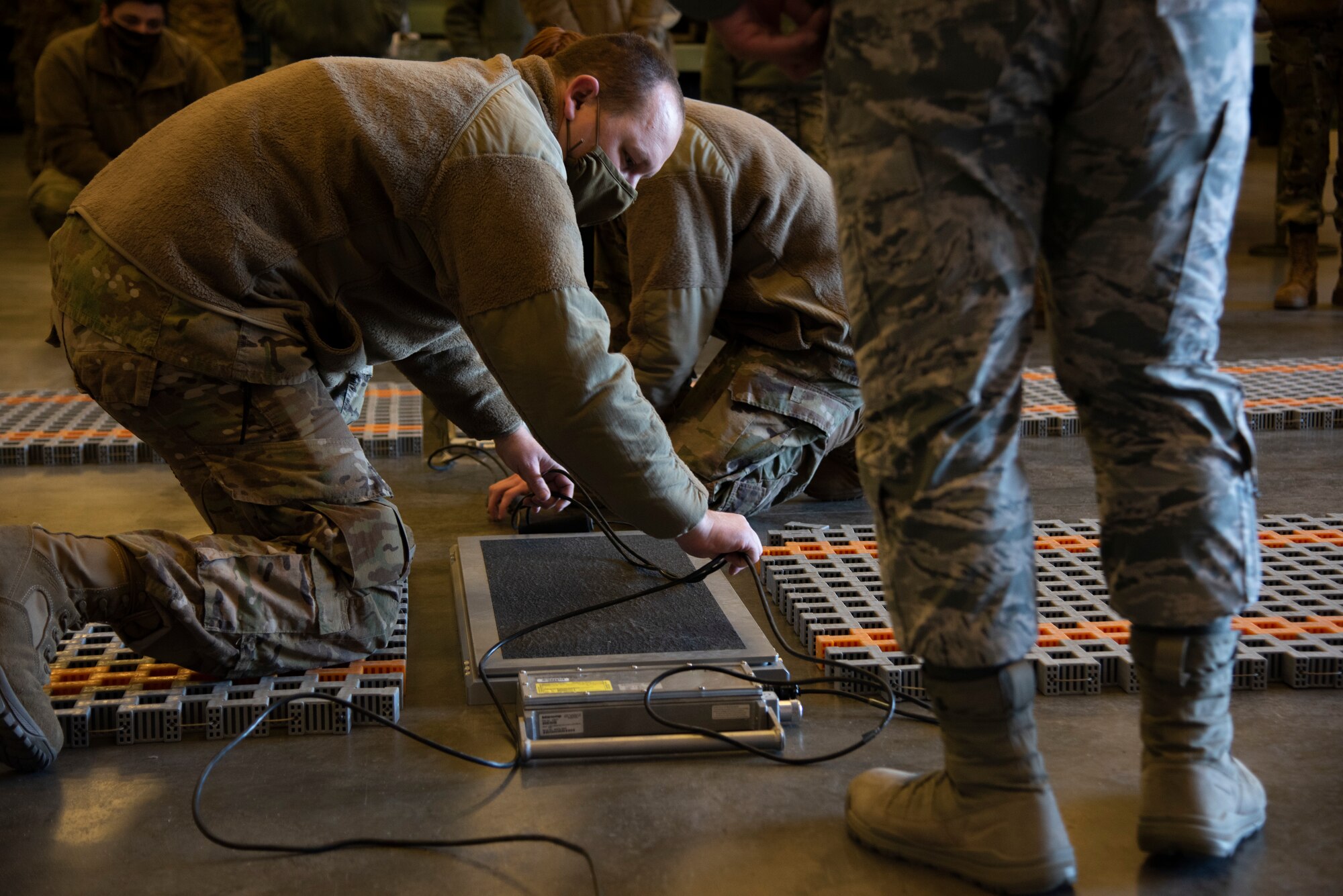 Airmen are kneeling on the ground to connecting wires to a scale
