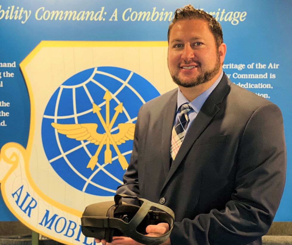 Program manager poses for a photo holding virtual reality goggles.