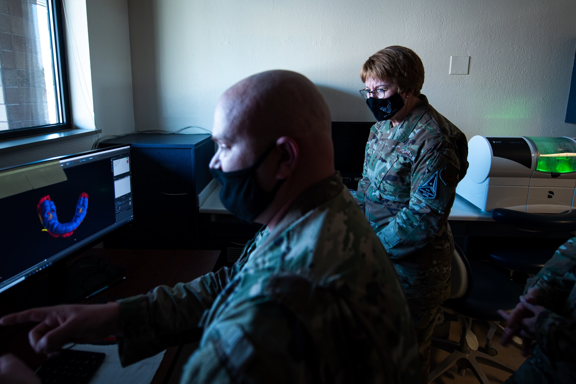 Two Airmen sit at a desk.