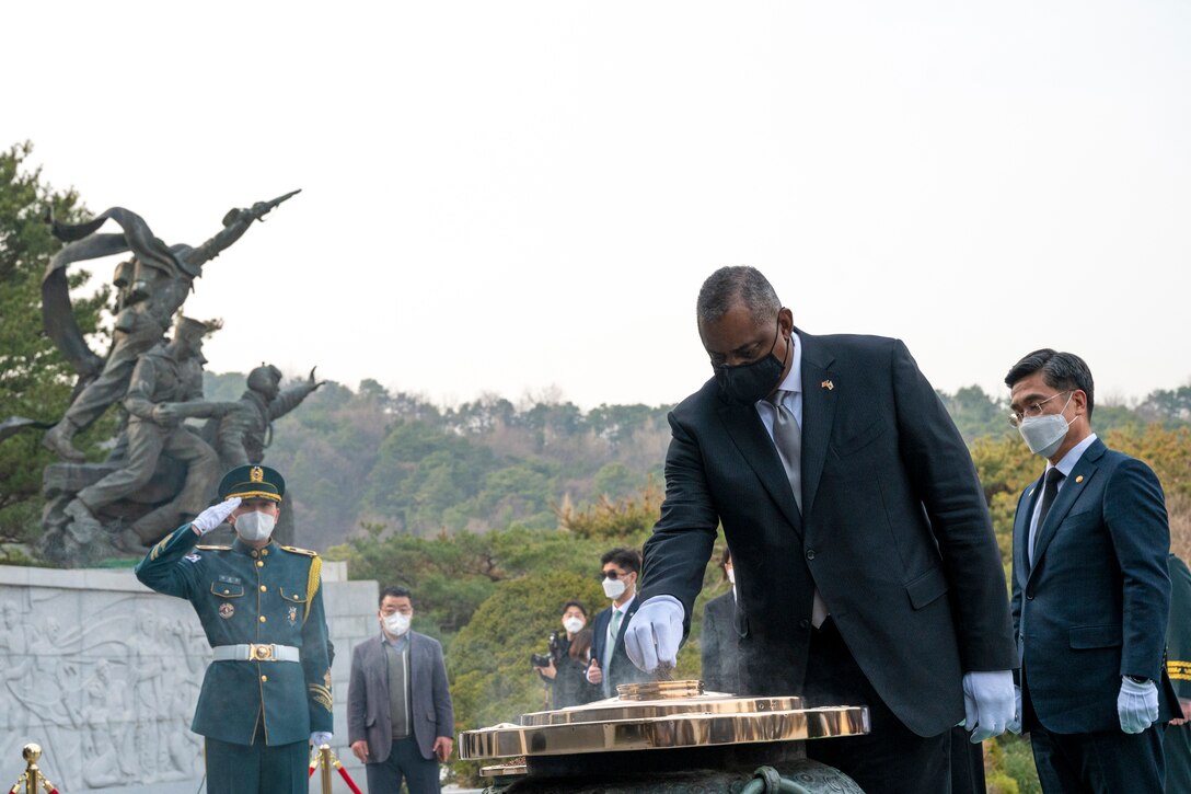 Secretary of Defense Lloyd J. Austin III handles incense at a cemetery as other officials stand nearby.