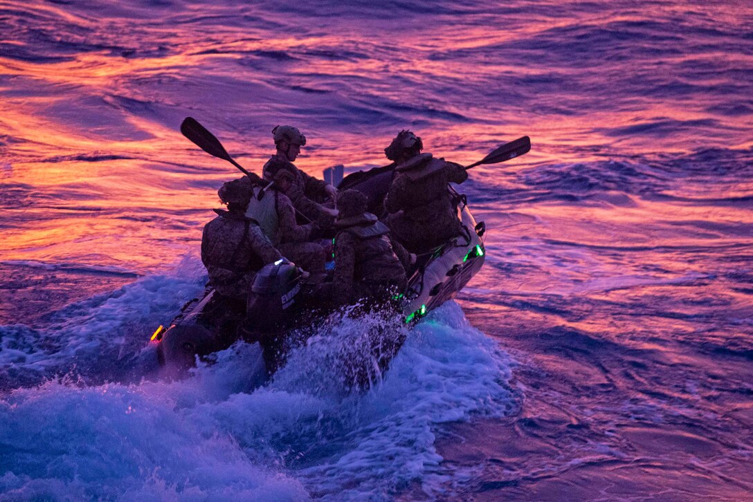 Marines and sailors paddle in an inflatable craft.