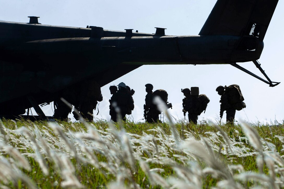 Marines walk into an aircraft as shown in silhouette through a field.
