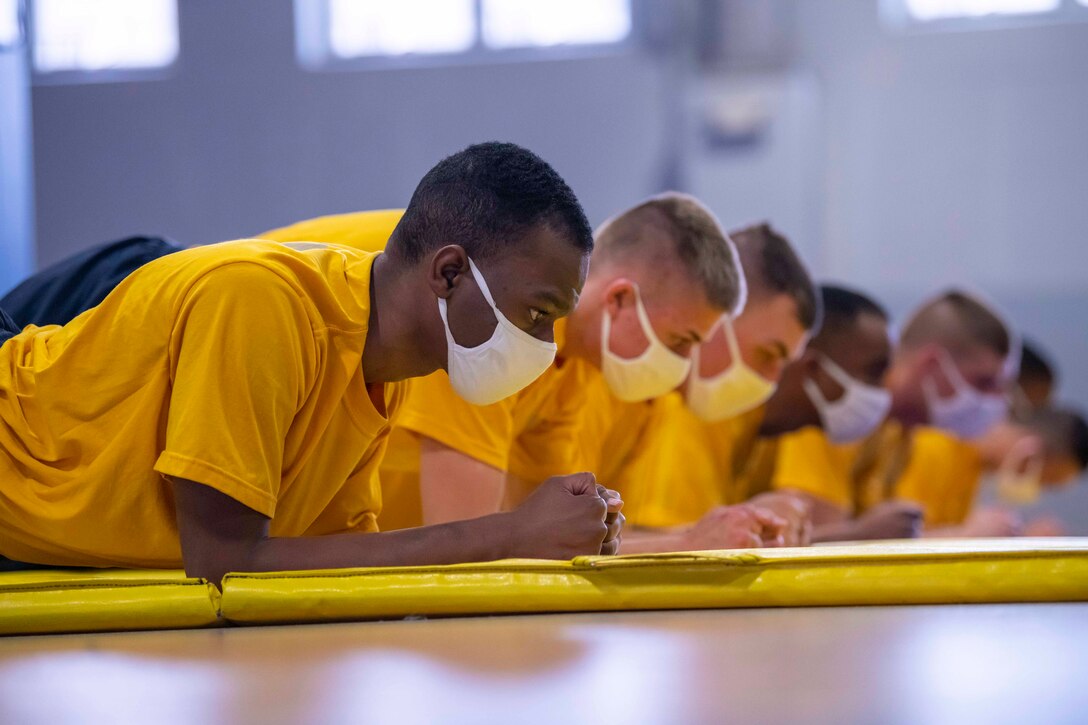 A group of Navy recruits assume plank positions.