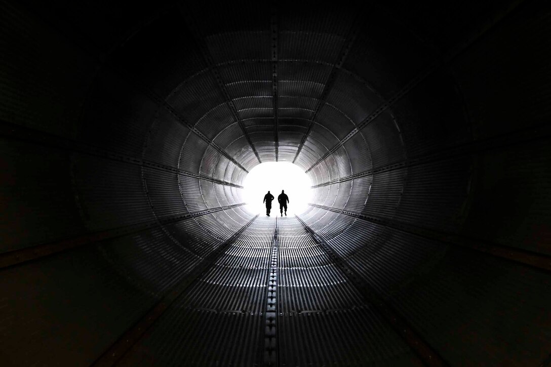 Two airmen shown in silhouette walk through a dark tunnel.