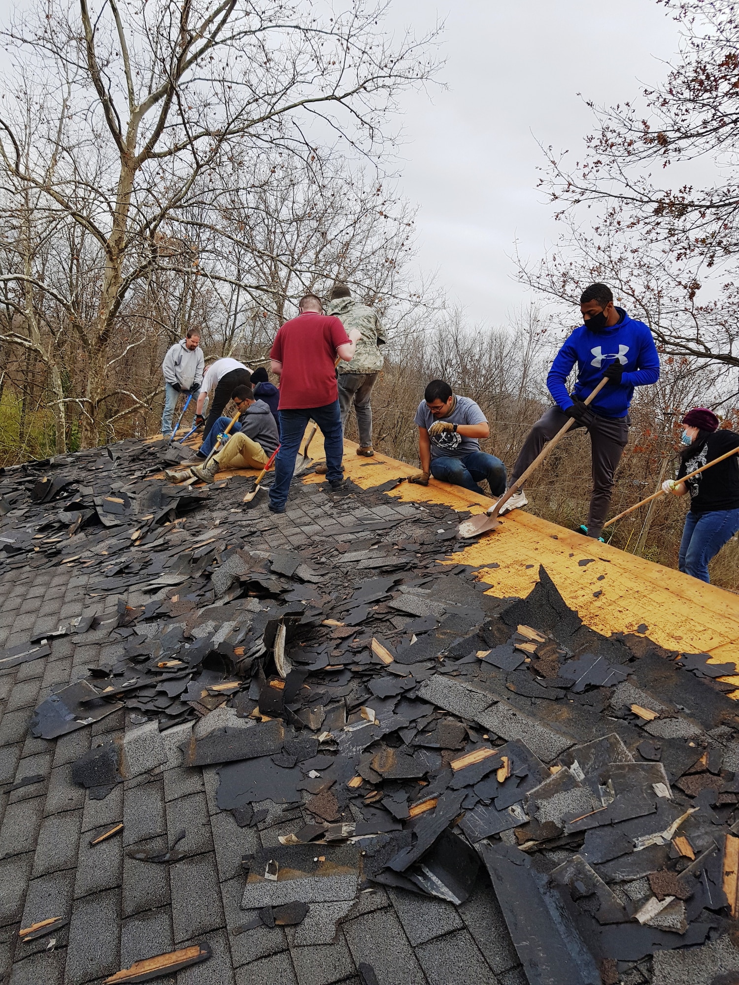 Volunteers scrape shingles off of a roof.