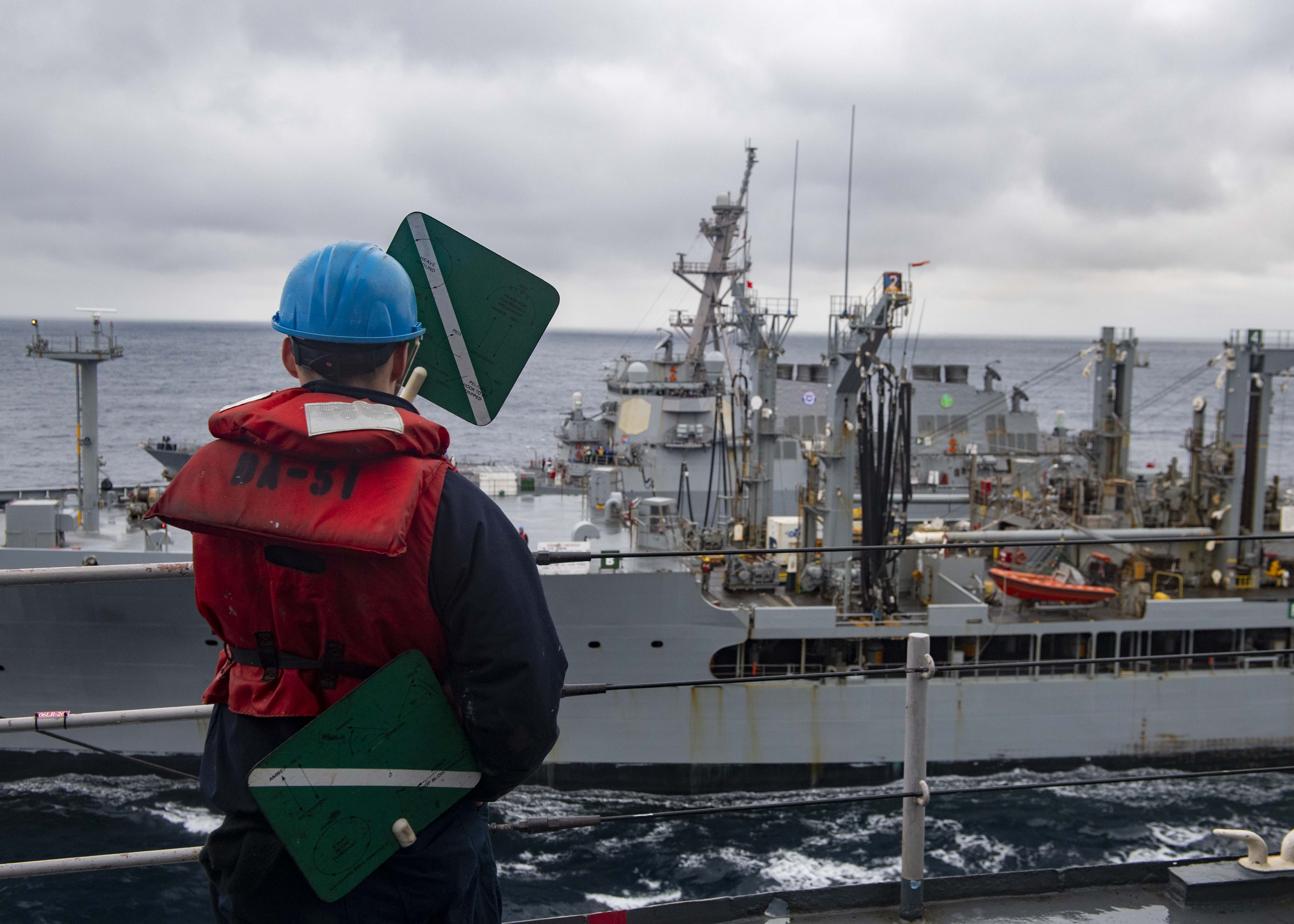 Seaman Cory Tremblay, assigned to the Harpers Ferry-class dock landing ship USS Carter Hall (LSD 50), signals to the crew of the Henry J. Kaiser-class fleet replenishment oiler USNS Lenthall (T-AO 189) during a replenishment-at-sea, March 17, 2021. C