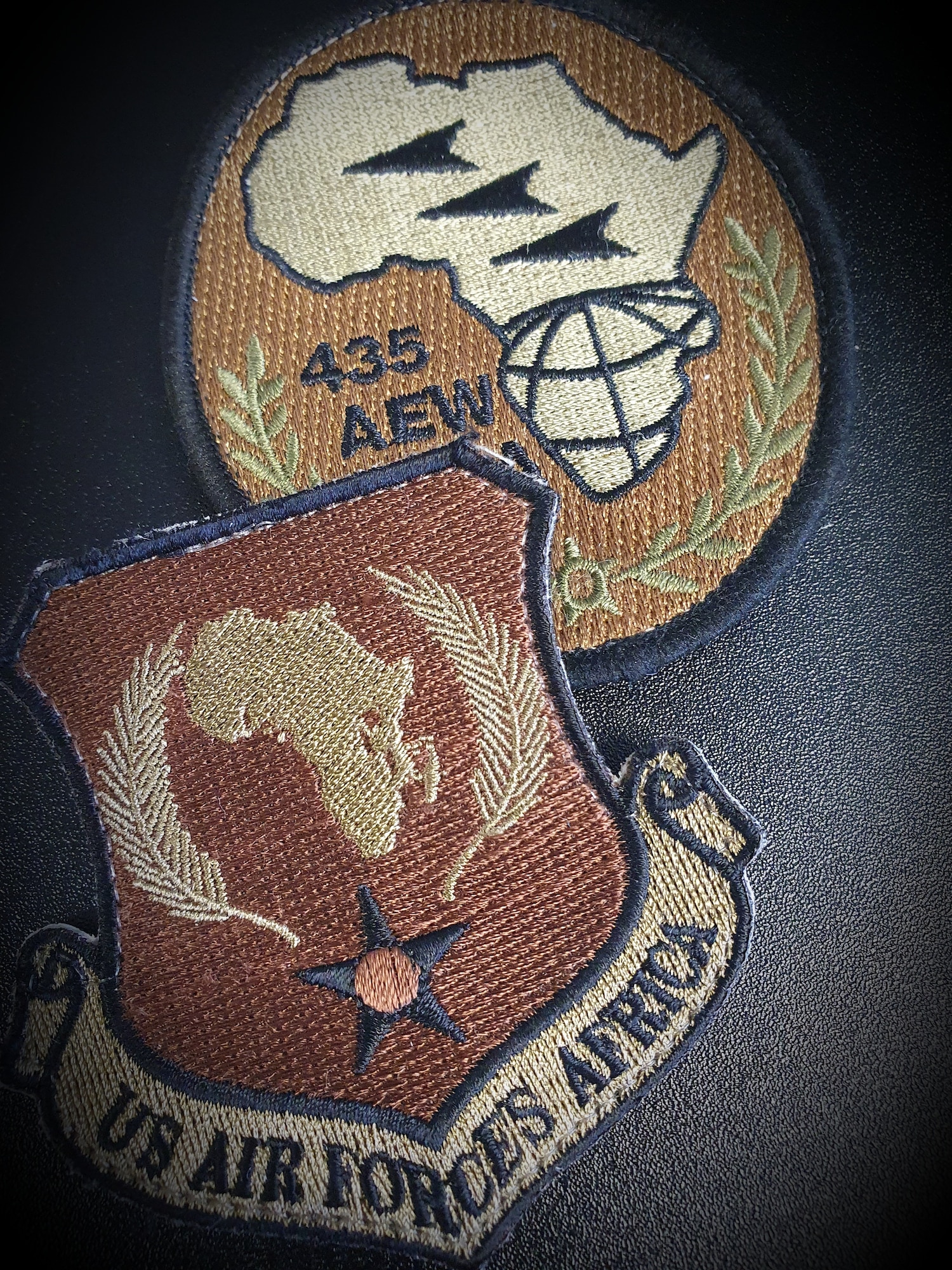 Patches for the United States Air Forces in Europe - Air Forces Africa and 435th Air Expeditionary Wing are displayed on a table at Ramstein Air Base, Germany, Mar. 19, 2021. Members of the 435 AEW are deployed throughout Africa supporting the U.S. Africa Command theater objectives. The 435 AEW is committed to protecting, developing and caring for Airmen. These Airmen are the reason the wing continues to succeed in accomplishing the mission better than its adversaries. (Courtesy illustration)