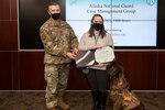 Maj. Gen. Torrence Saxe, adjutant general of the Alaska National Guard, left, awards Sweetface "Nyx" Shelton, a therapy dog, and her owner, Ashley Shelton, the Alaska Commendation Medal, Mar. 18, 2021, at Joint Base Elmendorf-Richardson, Alaska. Nyx provides emotional support to service members as part of the Sexual Assault Prevention and Response program and Warrior and Family Services.