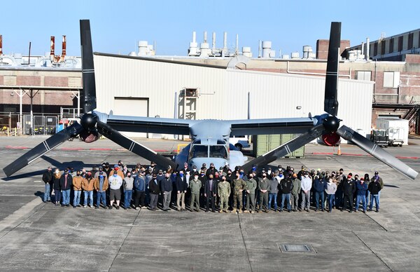 Group of aircraft maintenance professionals and officials pose in front of a V-22 Osprey