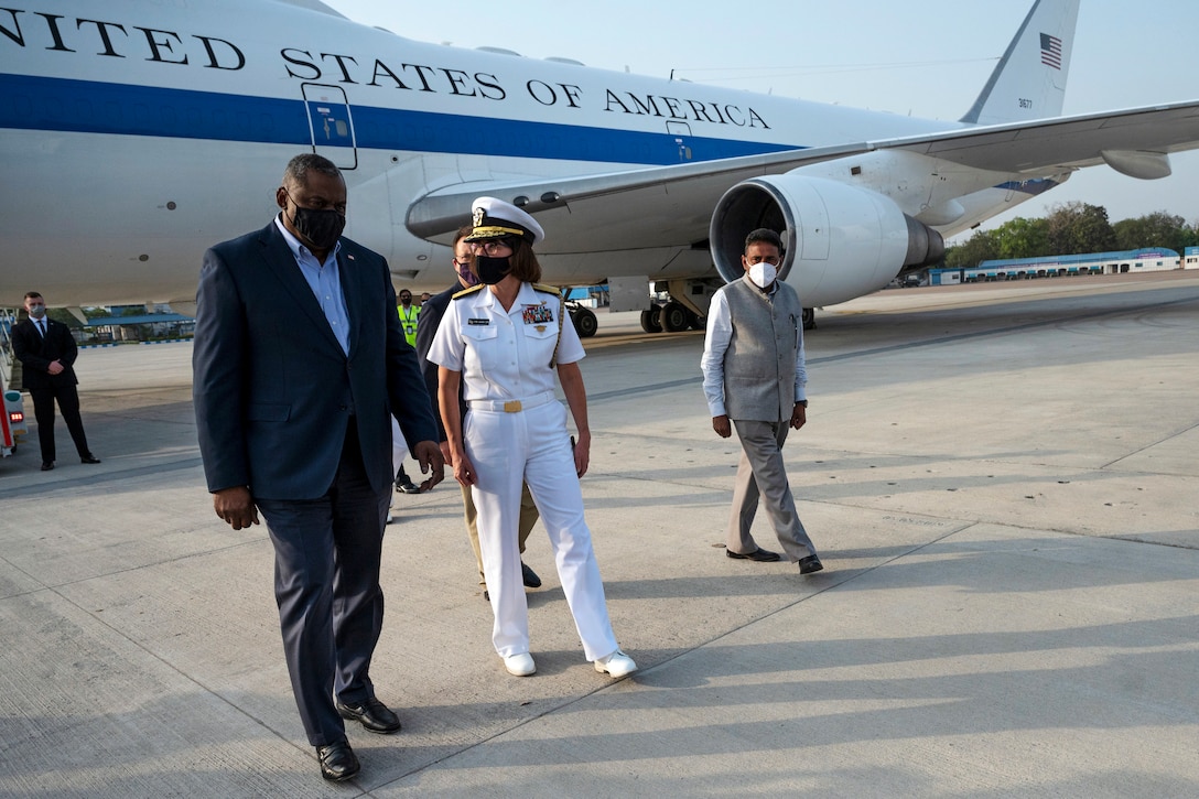 Secretary of Defense Lloyd J. Austin III walks with a service member and others with an aircraft in the background.