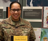 Senior Airman Yainna Hall poses for a photo near a display honoring Amelia Earhart in the Green Mountain Armory at Camp Johnson, Vermont, March 18, 2021. Hall, an aviation resource management specialist with the Vermont Air National Guard's 158th Operations Group, was one of several Soldiers and Airmen who showcased their uniforms and equipment for children at a Vermont day care center via teleconference. (U.S. Army National Guard photo by Don Branum)