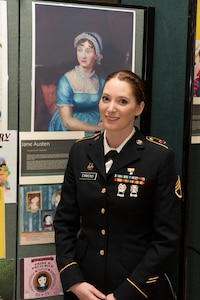 Army Staff Sgt. Trisha Emmons poses for a photo near a display of Jane Austen in the Green Mountain Armory on Camp Johnson, Vermont, March 18, 2021. Emmons, a human resources NCO with the Vermont Army National Guard's Medical Readiness Detachment, Garrison Support Command, was one of several Guardswomen who facilitated an online book reading and showcase of Guard uniforms and equipment for children at a local day care center. (U.S. Army National Guard photo by Don Branum)