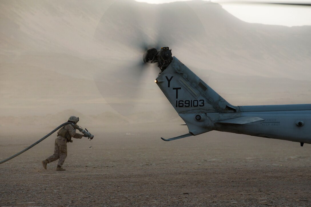 A Marine carries a fuel hose toward an aircraft in the desert.