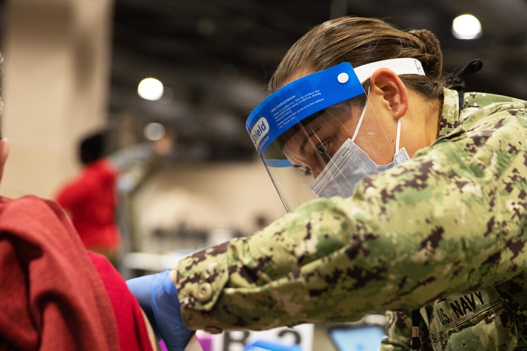 A sailor wearing a face mask administers a COVID-19 vaccine.