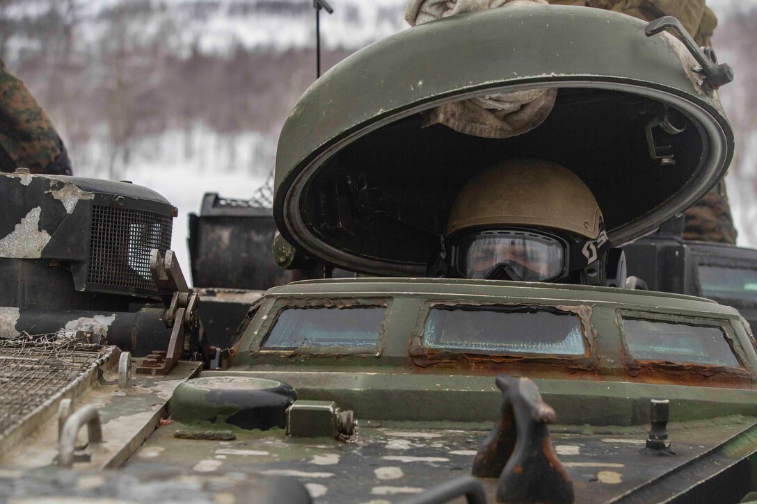 A Marine sits inside a military vehicle.
