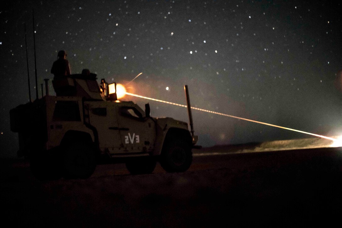 A Marine fires a machine gun from a vehicle under a starry sky.