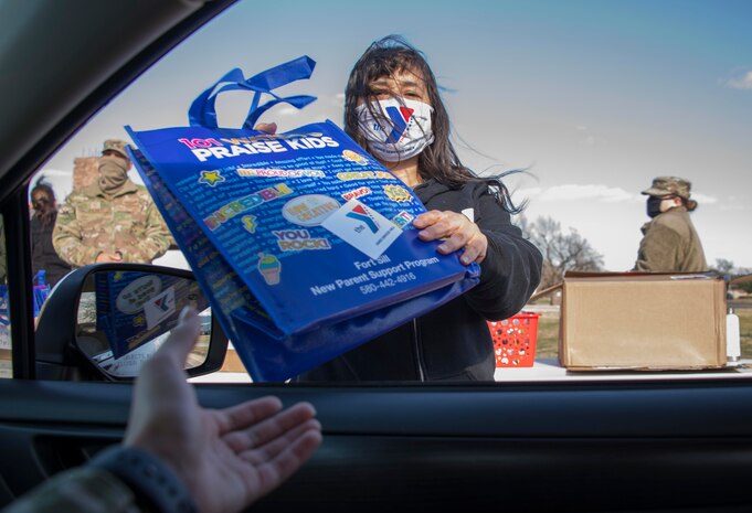 A member of the Armed Services YMCA (ASYMCA) of Altus Air Force Base (AFB) hands a welcome bag to an Airman during the ASYMCA open house drive-thru eventat Altus AFB, Oklahoma, March 18, 2021. The ASYMCA also handed out brochures that included information about various programs for Airmen and their families, including Operation Bring Baby Home, Hero’s Pantry, Airmen Against Drunk Driving,the Volunteer Program and more. (U.S. Air Force photo by Airman 1st Class AmandaLovelace)