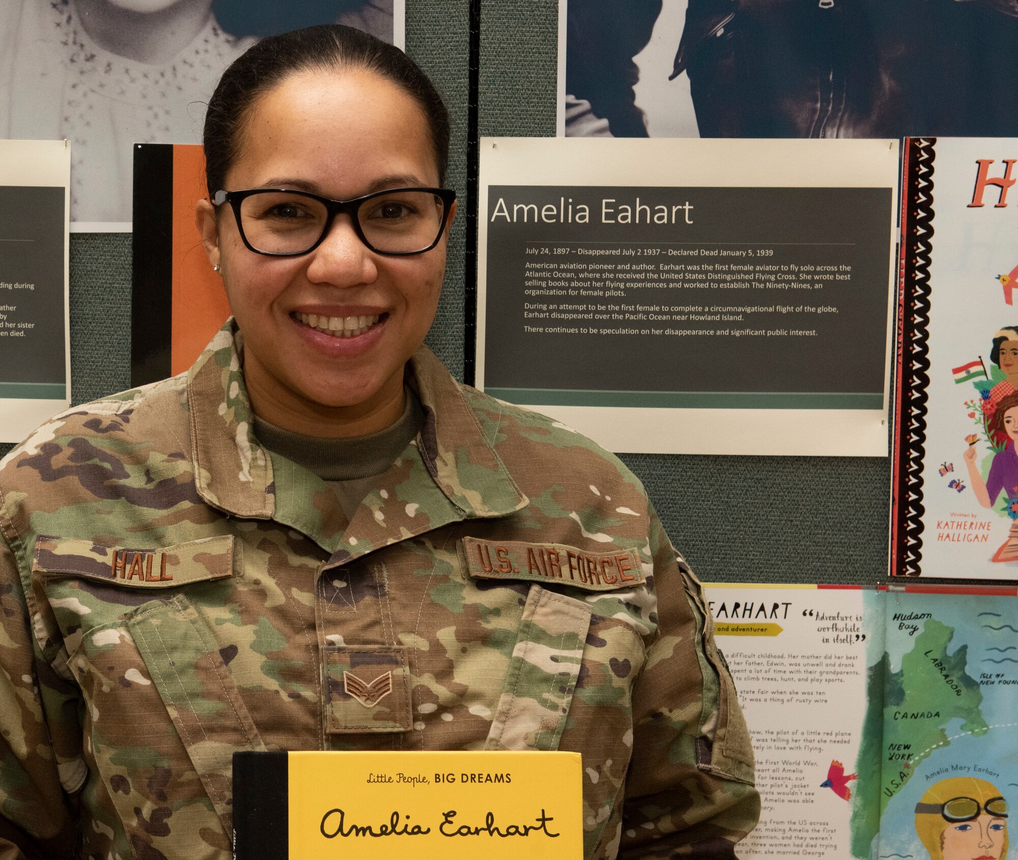 Senior Airman Yainna Hall, 158th Fighter Wing, Vermont Air National Guard, poses for a photo near a display honoring Amelia Earhart in the Green Mountain Armory at Camp Johnson, Vermont, March 18, 2021. Hall, an aviation resource management specialist with the Vermont Air National Guard's 158th Operations Group, was one of several Soldiers and Airmen who showcased their uniforms and equipment for children at a Vermont daycare center via teleconference.