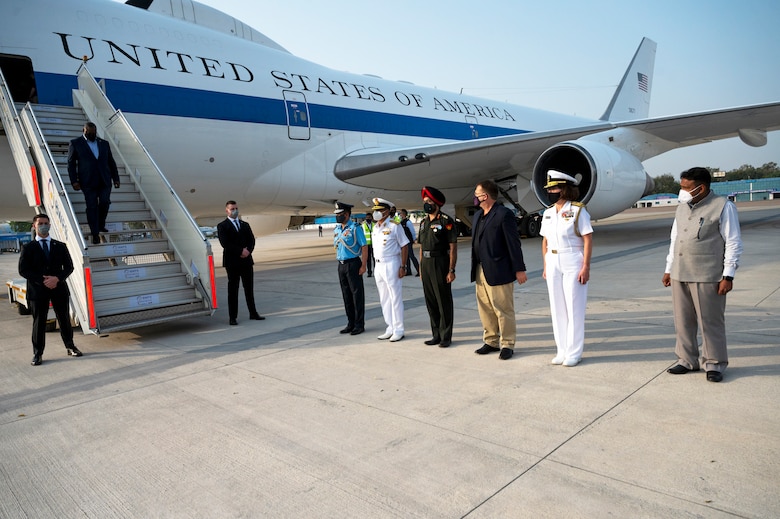 A man in business attire disembarks from an airplane bearing the words United States of America while six people stand in a line on the tarmac.